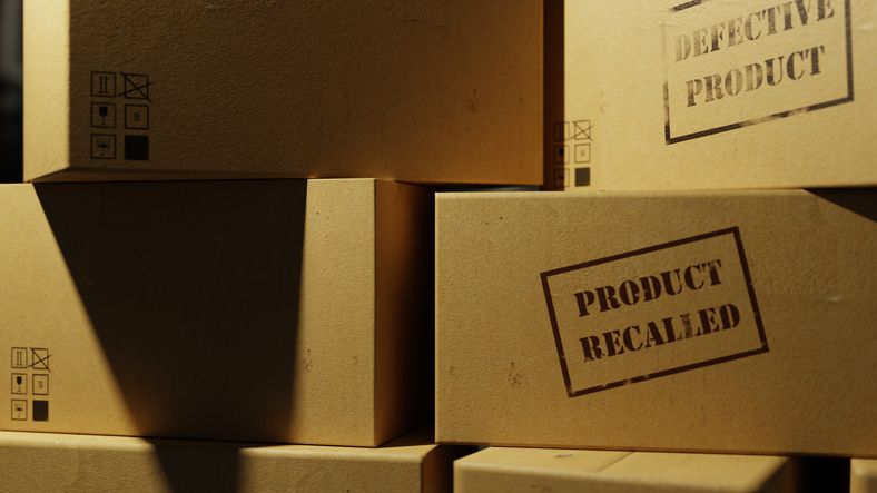A close-up of a pile of cardboard boxes stamped with "Product Recalled" and "Defective Product."