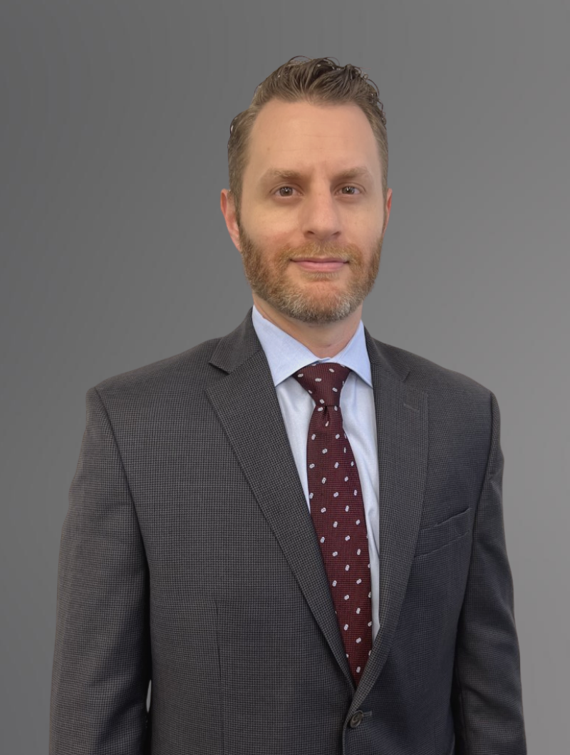 Attorney Evan Able in a grey suit with light blue shirt and maroon tie & grey background